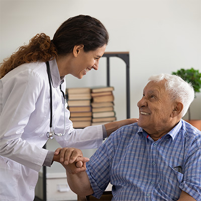 Nurse leaning down to speak with a resident while holding his hand.